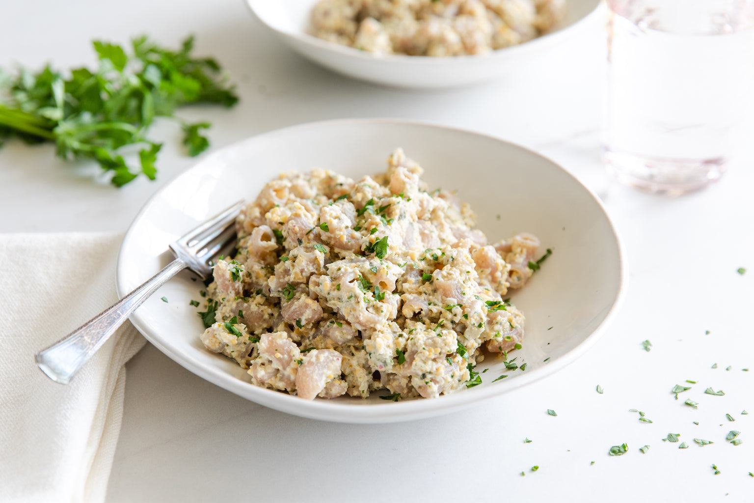 Bowl of vegan chickpea “tuna” salad served with a fork on a white table, garnished with chopped parsley