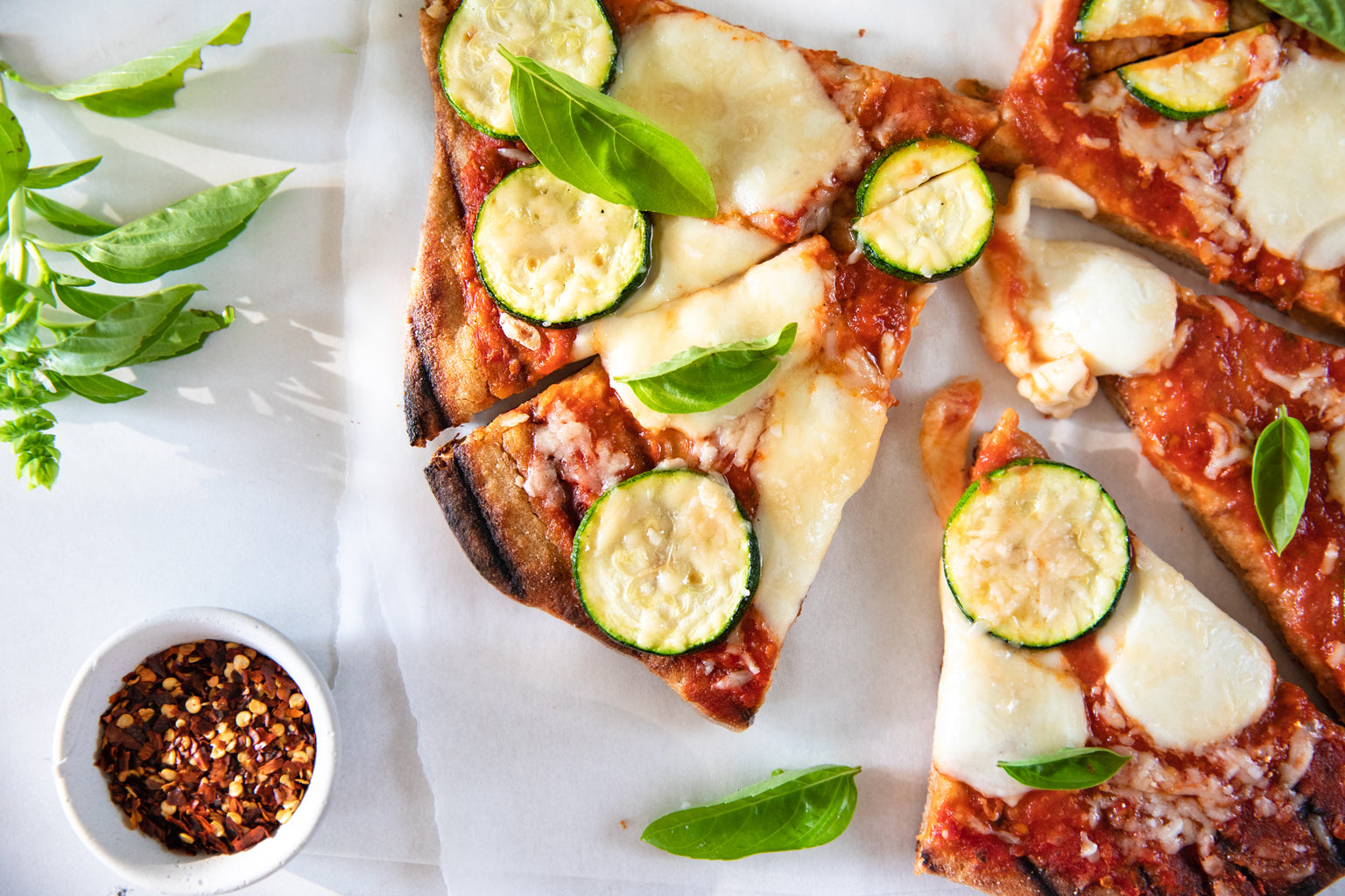 Grilled whole-wheat einkorn pizza slices topped with mozzarella, zucchini and basil, with red pepper flakes