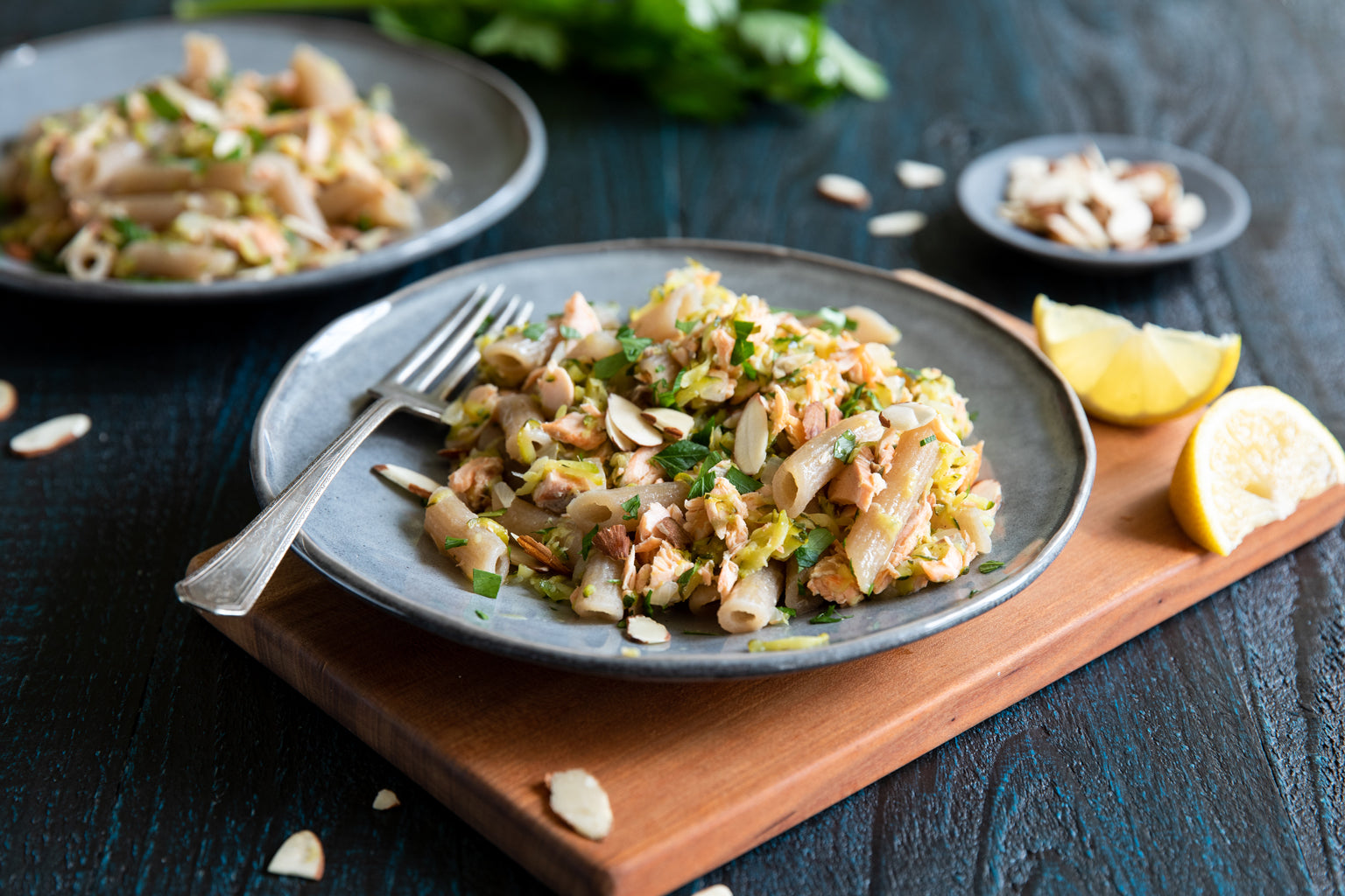 Plate of cassava pasta with flaked salmon, zucchini, sliced almonds, and lemon wedge on a wooden board