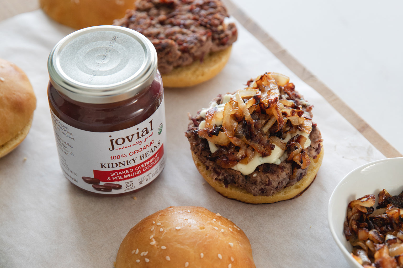 Jovial jar of organic kidney beans beside a grilled kidney-bean burger topped with cheese and caramelized onions