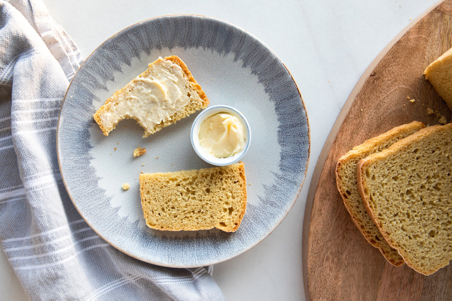Top-down view of Beginner Einkorn Bread slices showcasing butter spread on one slice with a ceramic plate and wooden cutting board background