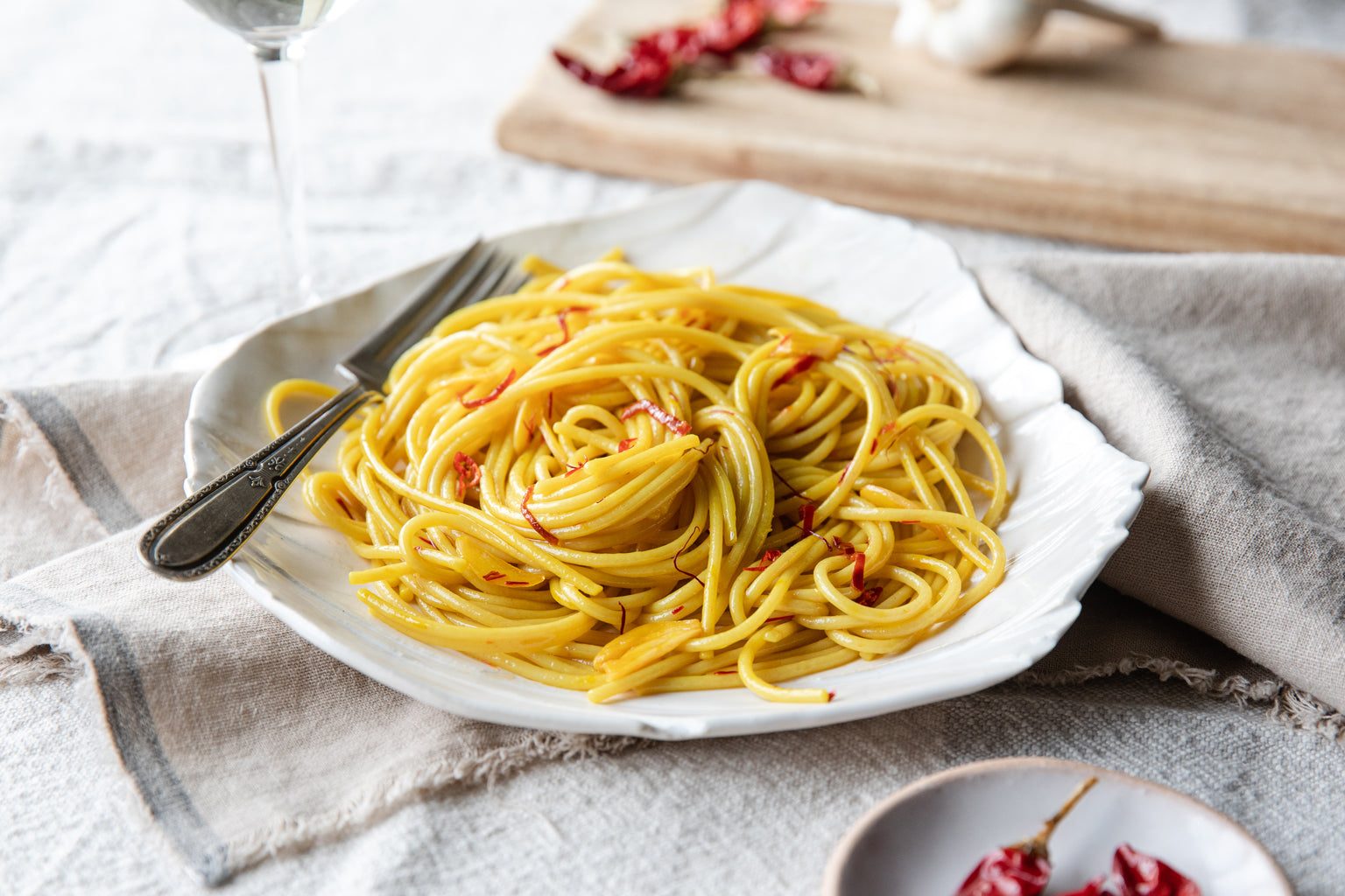 Italian saffron aglio e olio spaghetti twirled into nests on a white plate with a fork on a linen napkin