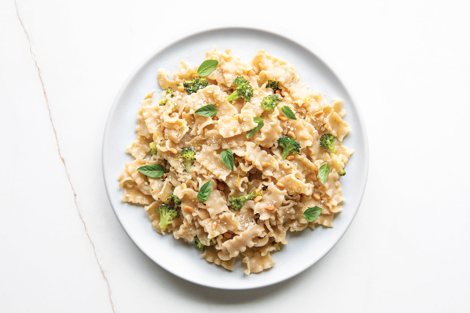 Mafalda pasta tossed with broccoli, lemon zest, pine nuts and basil on a white plate