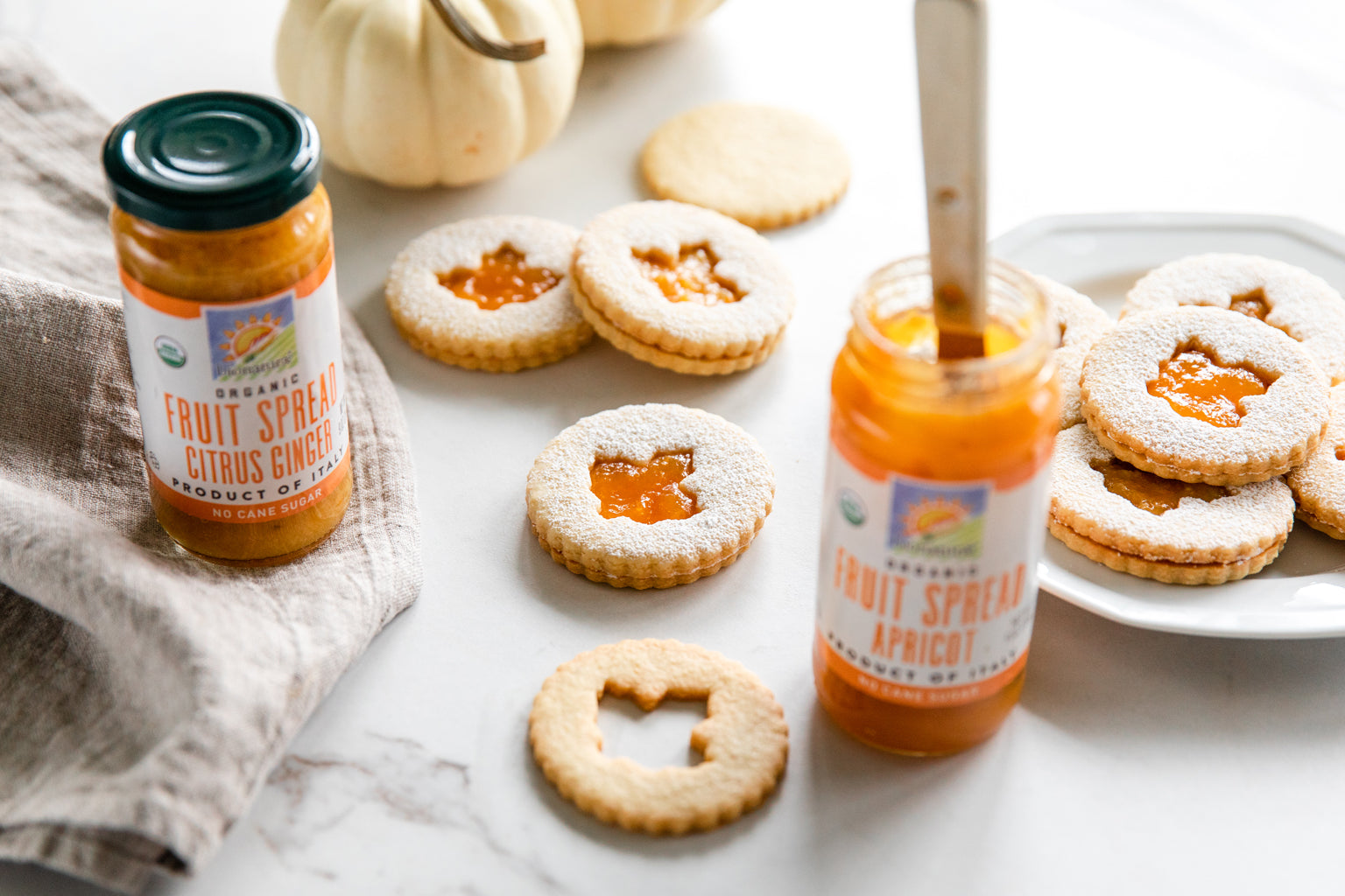 Einkorn Linzer cookies dusted with powdered sugar, filled with bionaturae apricot and citrus ginger spreads beside jars