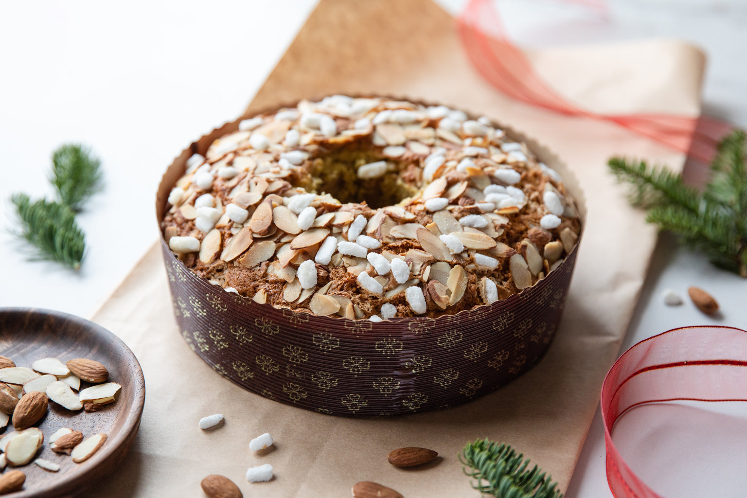 Three-quarter view of Einkorn Italian Christmas cake with sliced almonds and pearl sugar in a paper mold on parchment