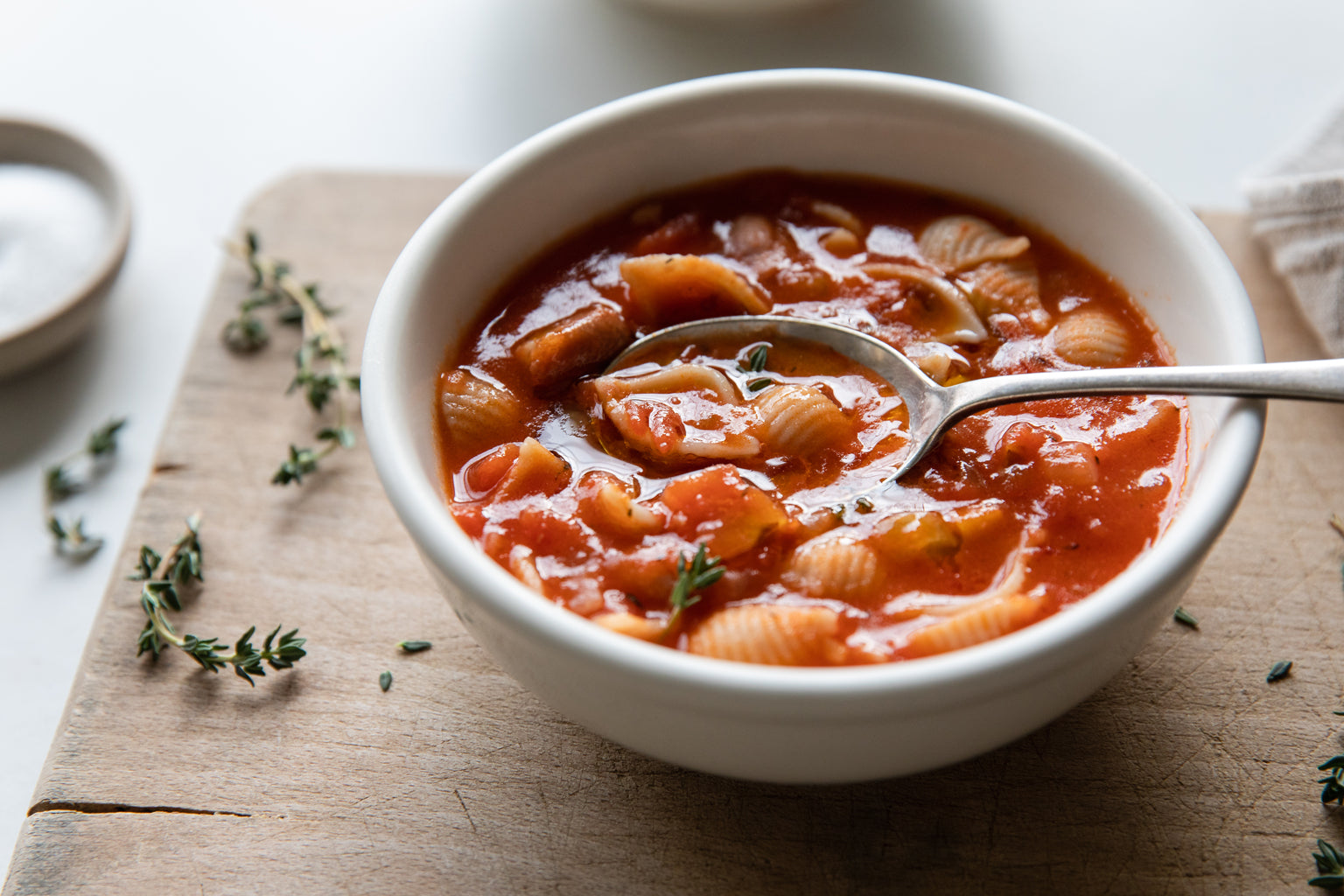 Bowl of Italian pasta e fagioli soup with shell pasta in tomato broth, spoon in bowl on a wooden board with thyme sprigs