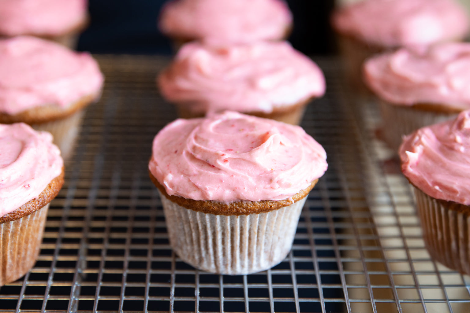 Close-up of an Einkorn strawberry cupcake showcasing pink strawberry frosting and golden-brown cake on a cooling rack