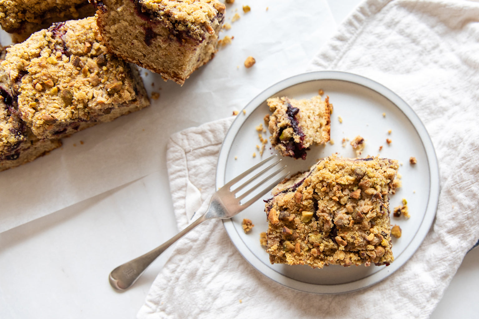 Overhead view of an Einkorn cherry pistachio coffee cake slice showing pistachio streusel and cherry filling on a white plate with a fork