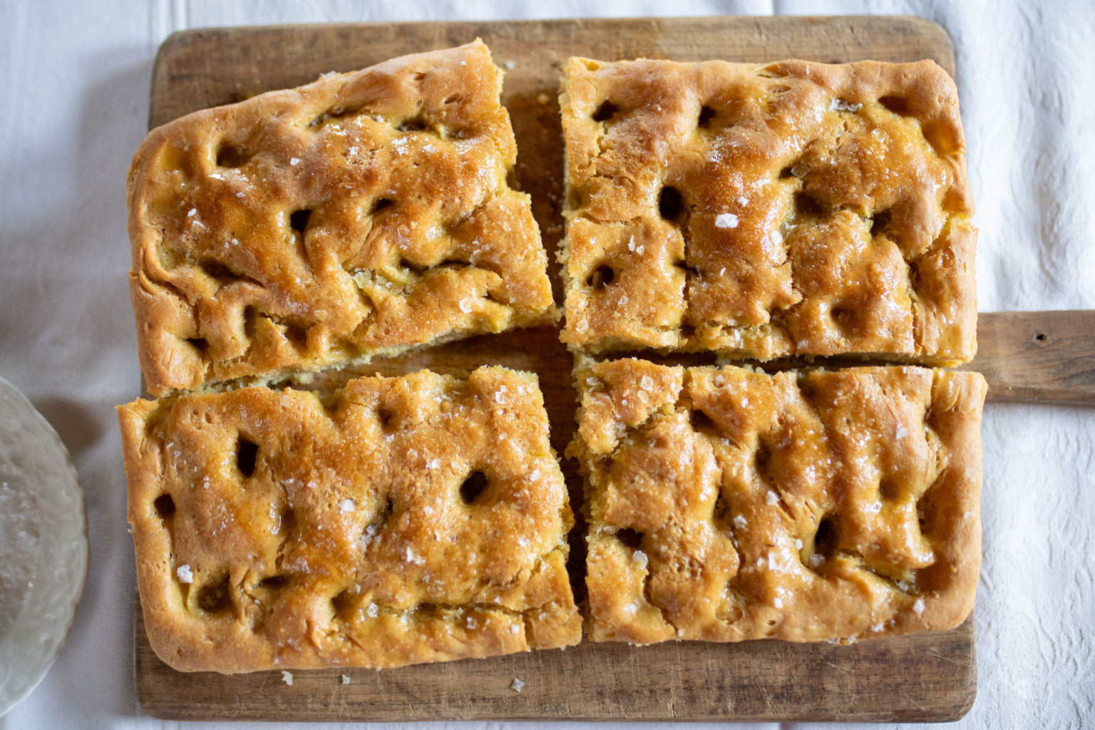 Top down view of Einkorn focaccia cut into four squares showcasing dimpled golden crust and coarse salt on a wooden board