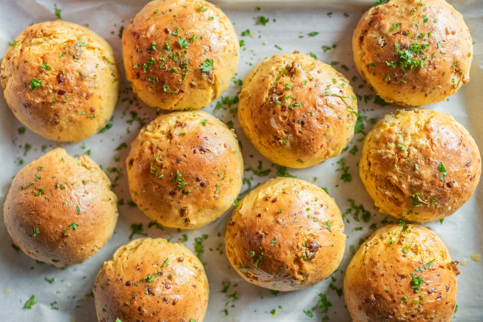 Top-down view of Einkorn dinner rolls with sausage and cheese on parchment-lined tray sprinkled with parsley