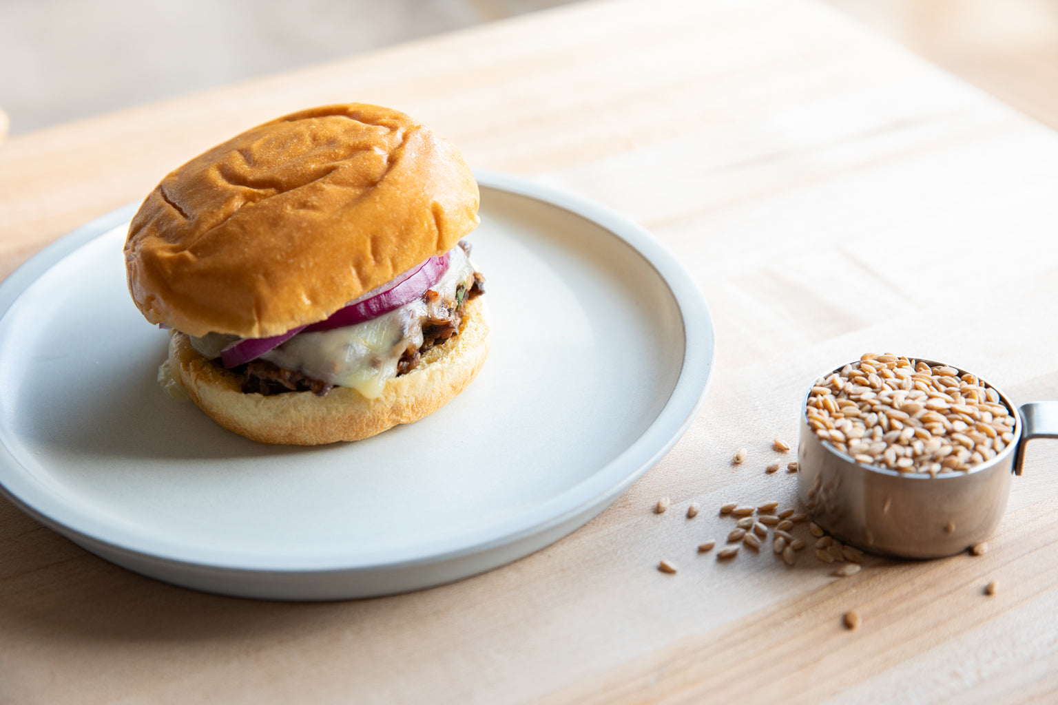 Wheat berry and black bean burger with melted cheese and red onion on a white plate, cup of wheat berries on wood