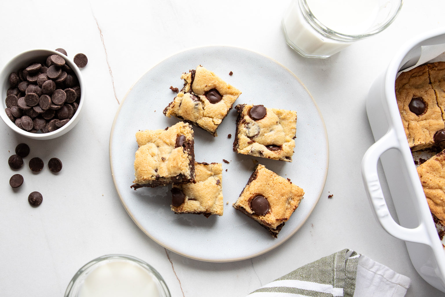 Overhead view of Einkorn brookies with chocolate chip cookie tops and brownie layer on white plate, baking dish, and milk