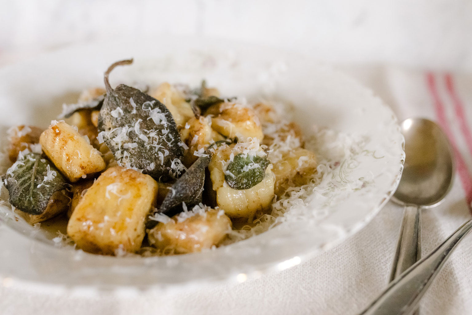 Ricotta einkorn gnocchi tossed in browned butter and sage on a white vintage plate with grated cheese and a spoon at the side