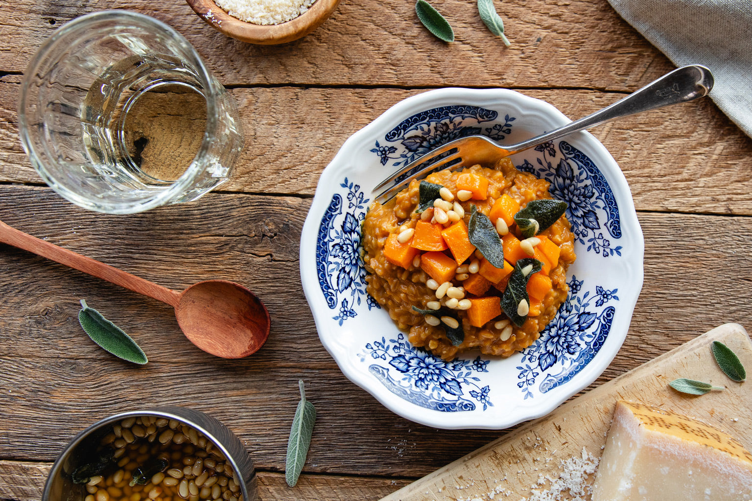 Butternut squash and sage wheat berry risotto in a blue patterned bowl on a wooden table with pine nuts and cheese