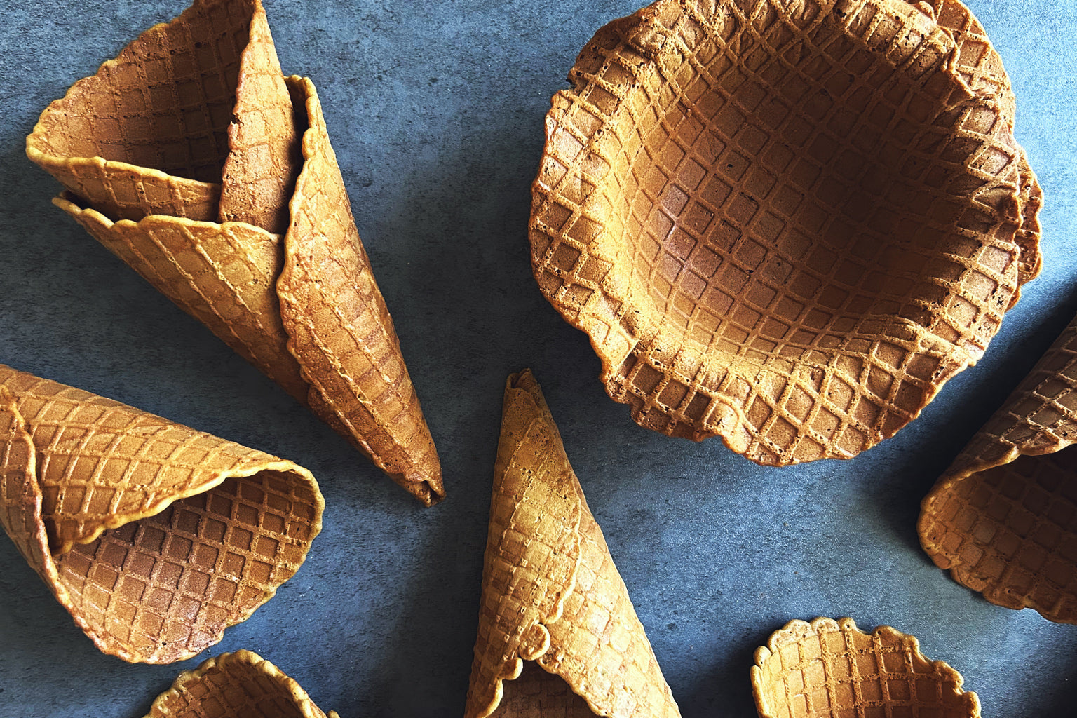 Overhead view of Einkorn sourdough ice cream waffle cones and a waffle bowl showing crisp waffle texture on a dark slate background