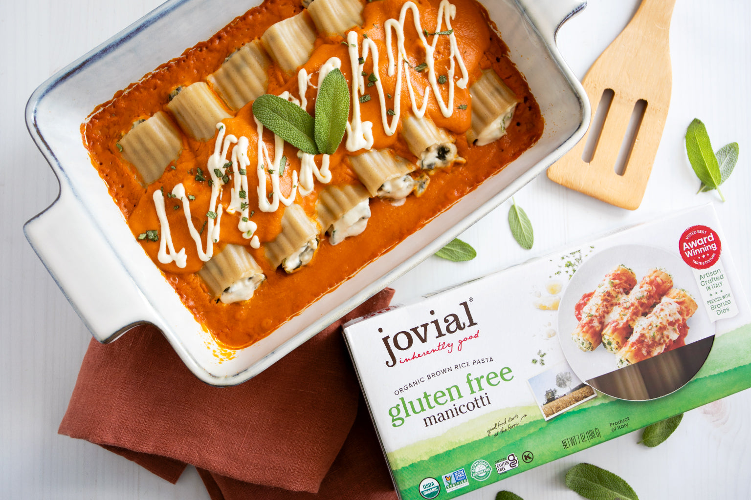Baked pumpkin sage brown rice manicotti in a white baking dish with tomato sauce, sage garnish and Jovial gluten free box