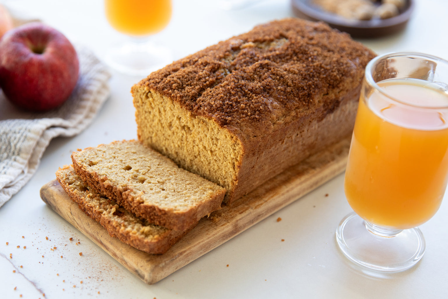 Sliced Einkorn apple cider loaf cake on a wooden board with a glass of apple cider