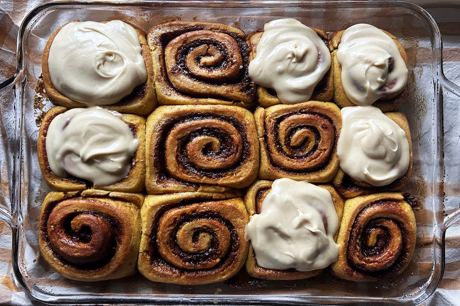 Overhead view of Einkorn sourdough pumpkin cinnamon rolls in a glass pan, some topped with maple cream cheese frosting