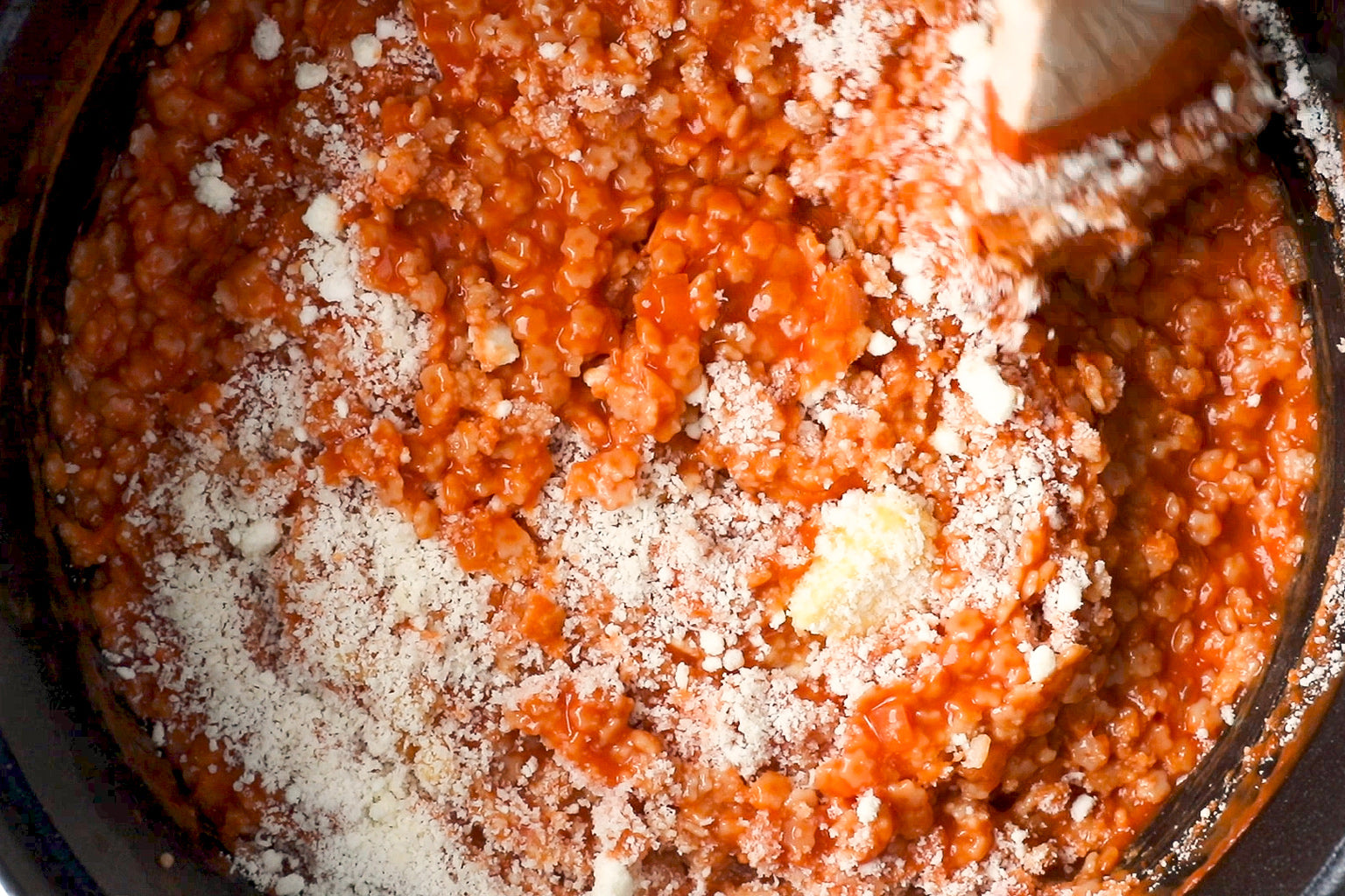 Stelline pasta simmering in tomato pomodoro sauce topped with grated Parmesan, wooden spoon in pot