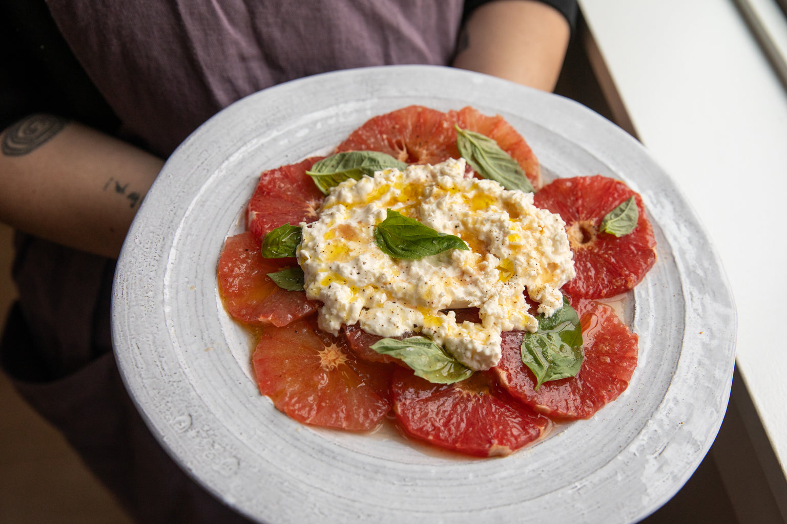 Overhead view of grapefruit and burrata salad with sliced grapefruit, creamy burrata, basil leaves, and olive oil on a white plate