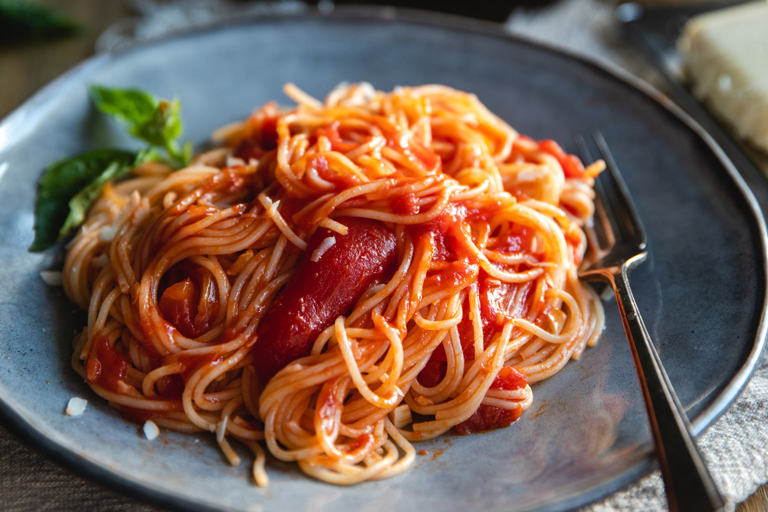 Capellini pasta tossed with tomato fillets on a blue plate with basil and a fork