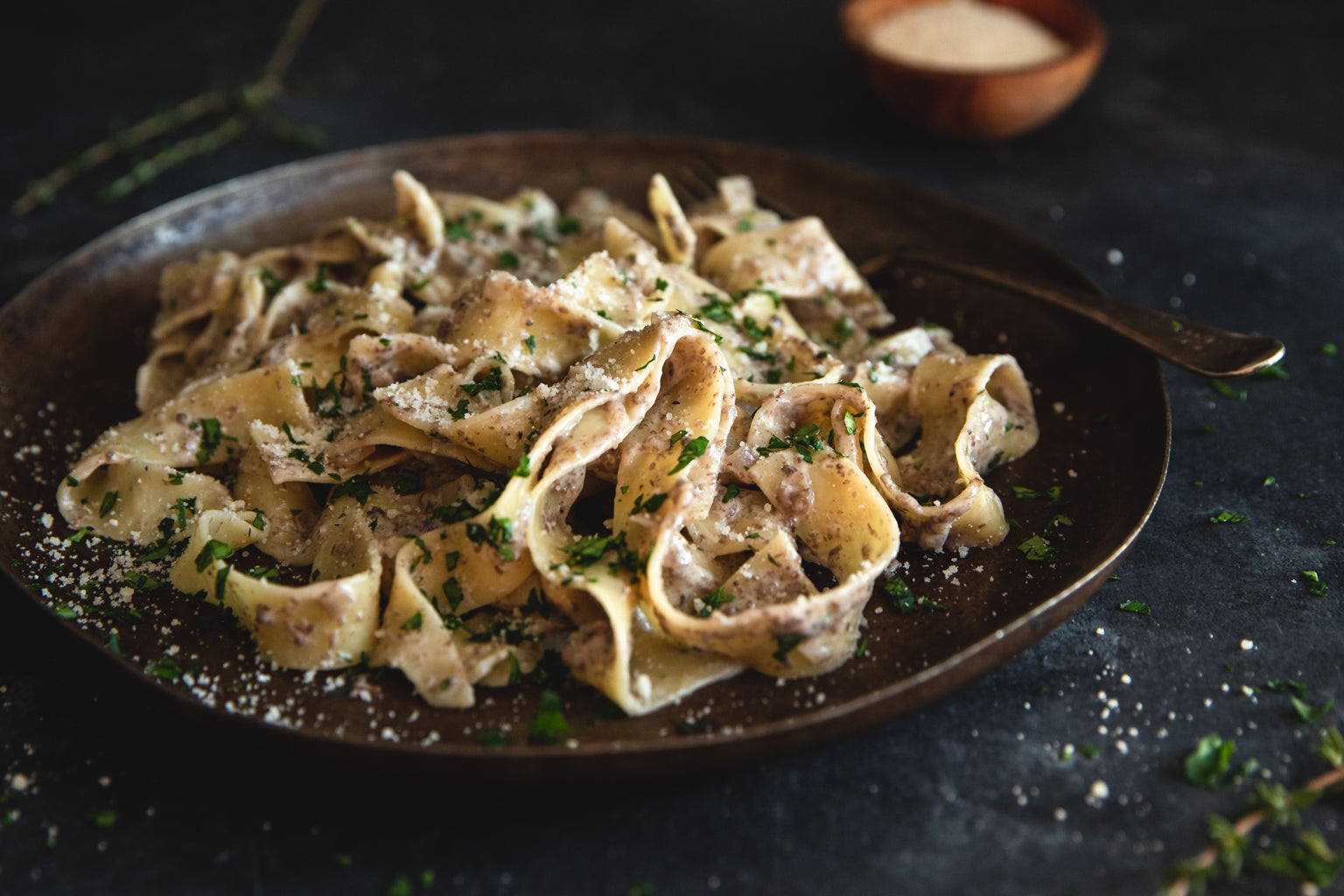 Pappardelle tossed in a creamy mushroom sauce on a dark plate, garnished with grated cheese and chopped parsley