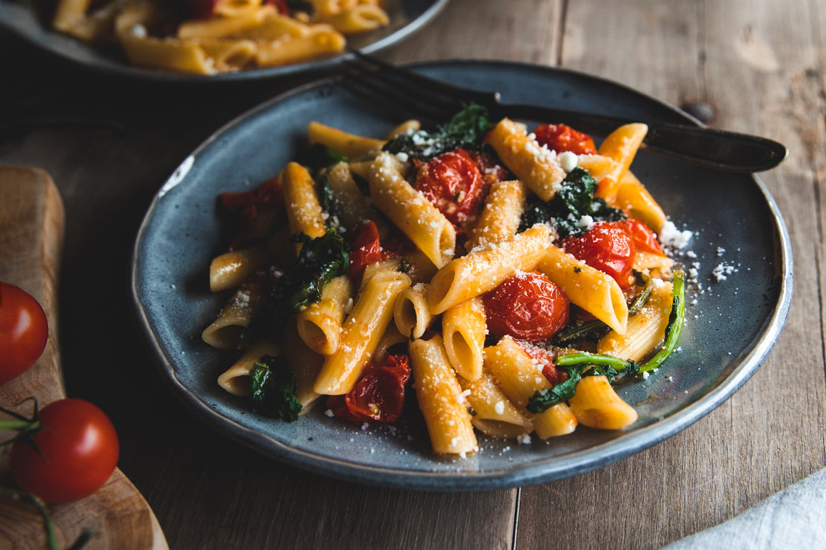 Penne with garlicky broccoli rabe and roasted cherry tomatoes served on a ceramic plate on a rustic wooden table