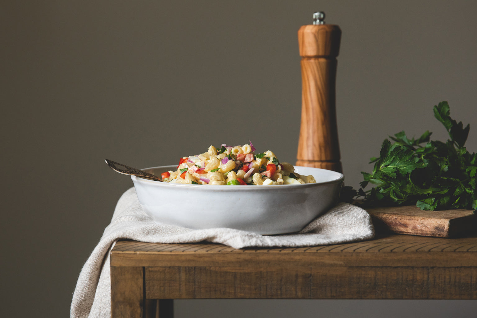 Bowl of gluten-free macaroni salad served on a wooden table with a pepper mill and fresh parsley
