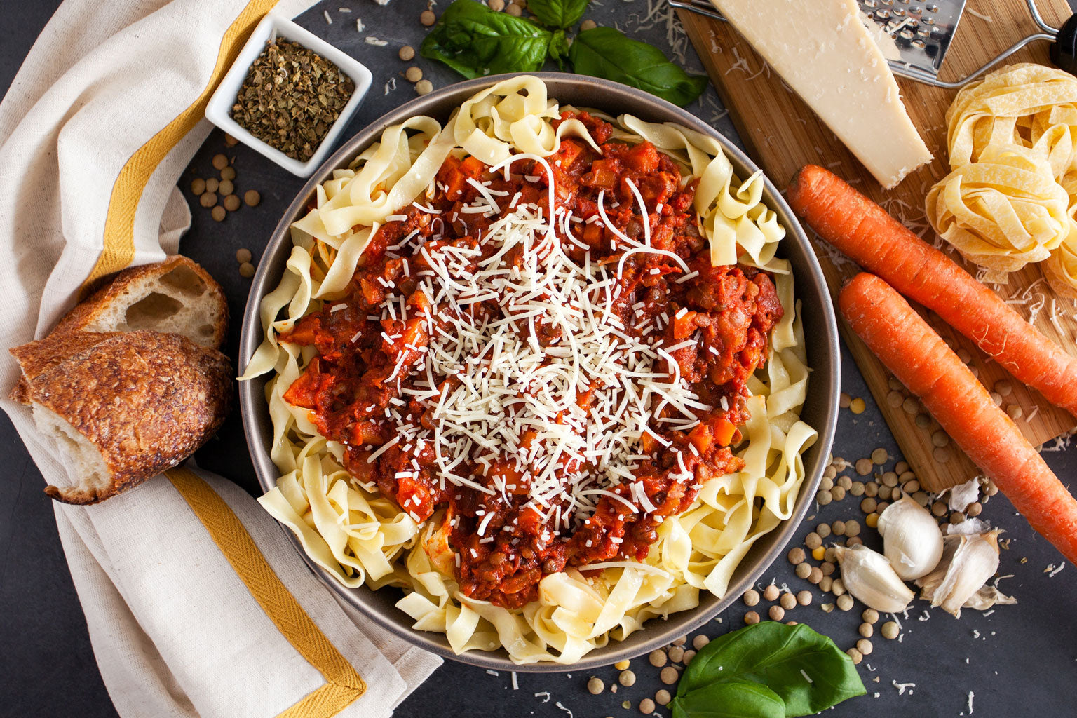 Bowl of vegetarian lentil bolognese over ribbon pasta with grated cheese, bread and basil
