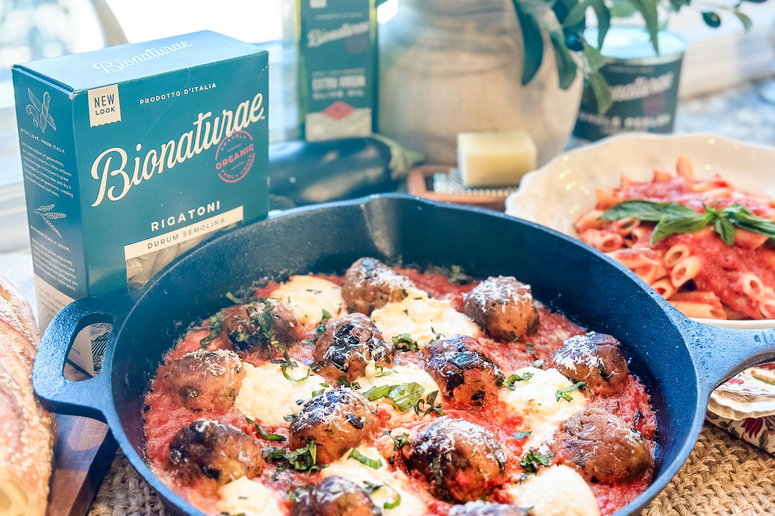 Eggplant meatballs simmering in marinara in a cast-iron skillet, with a bowl of pasta and a Bionaturae rigatoni box