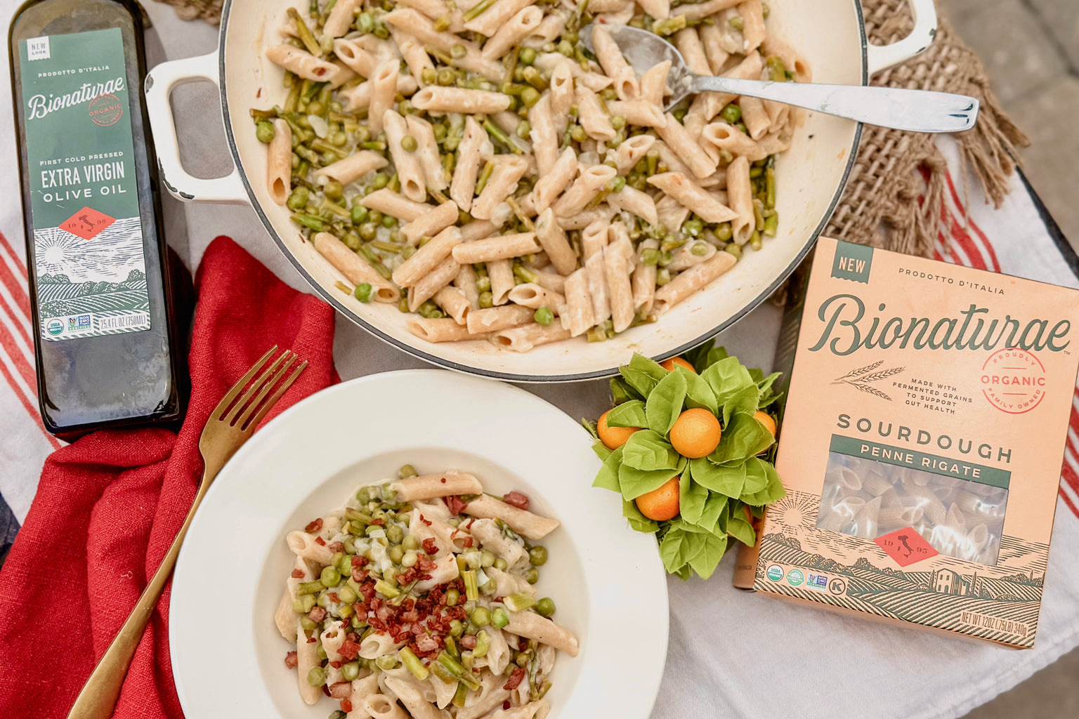 Bowl of sourdough penne with asparagus and peas, skillet of pasta, Bionaturae sourdough penne box and bottle of extra virgin olive oil