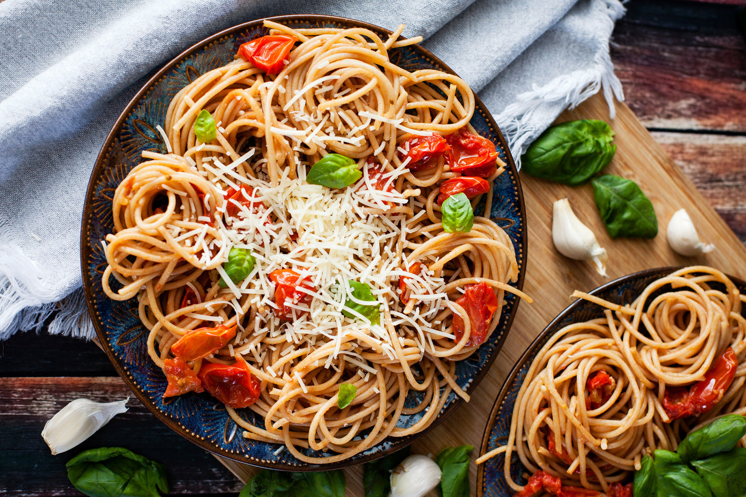 Whole wheat spaghetti alla checca with roasted cherry tomatoes, fresh basil and grated cheese on a blue plate on a wooden board