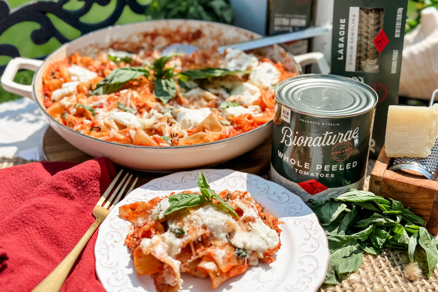 Skillet lasagna on a white plate beside the pan and a Bionaturae can of whole peeled tomatoes outdoors