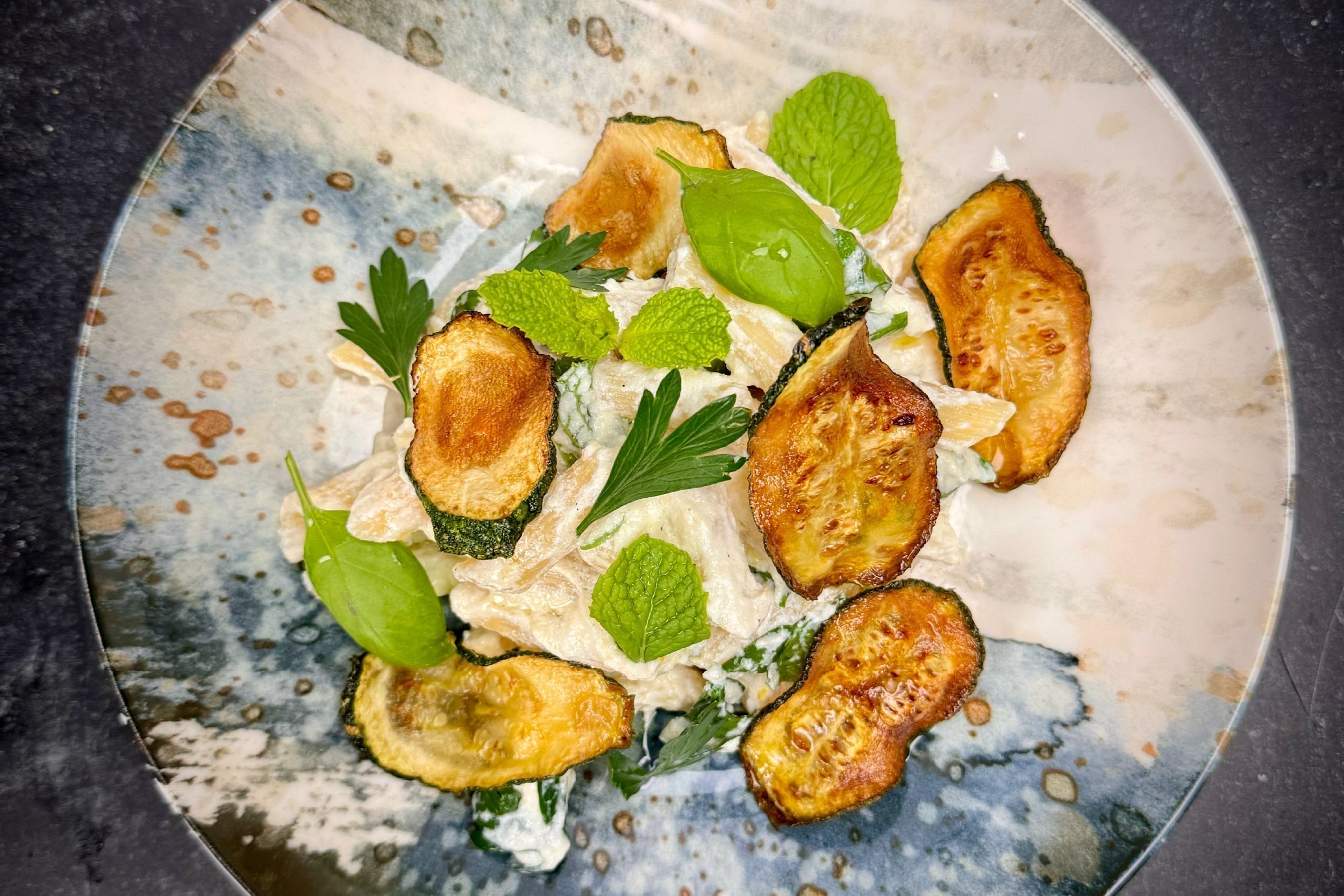 Penne tossed in creamy ricotta-lemon sauce topped with fried zucchini chips and fresh herbs on a rustic ceramic plate