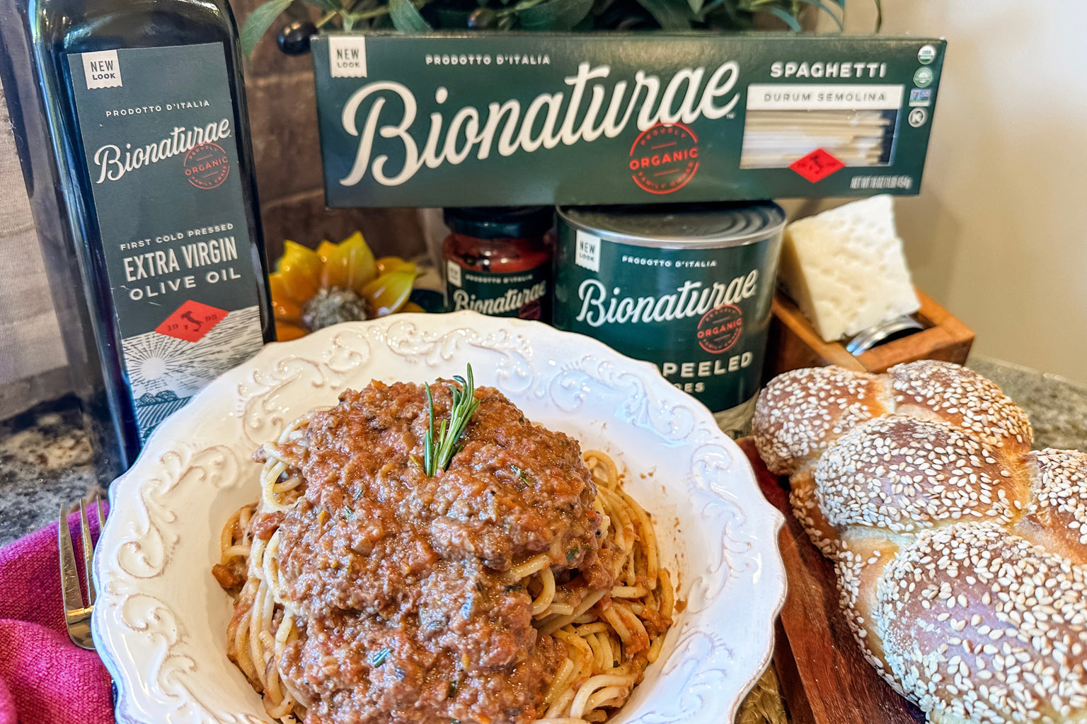Bowl of spaghetti with mushroom bolognese, Bionaturae pasta and olive oil cans behind it, sesame rolls on a wooden board