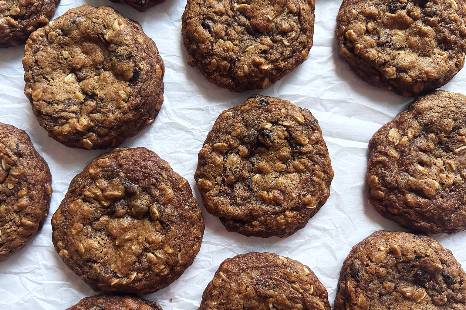 Overhead view of sourdough einkorn oatmeal raisin cookies showcasing oats and raisins on crinkled parchment paper