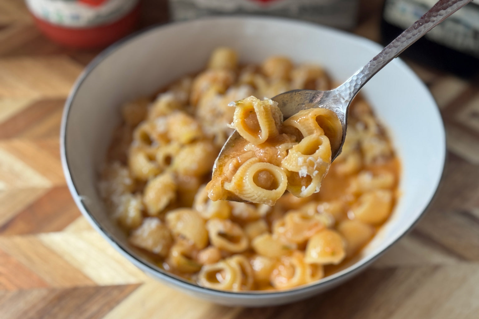 Fork lifting shell pasta from a bowl of Pasta e Ceci (pasta and chickpeas) on a wooden cutting board