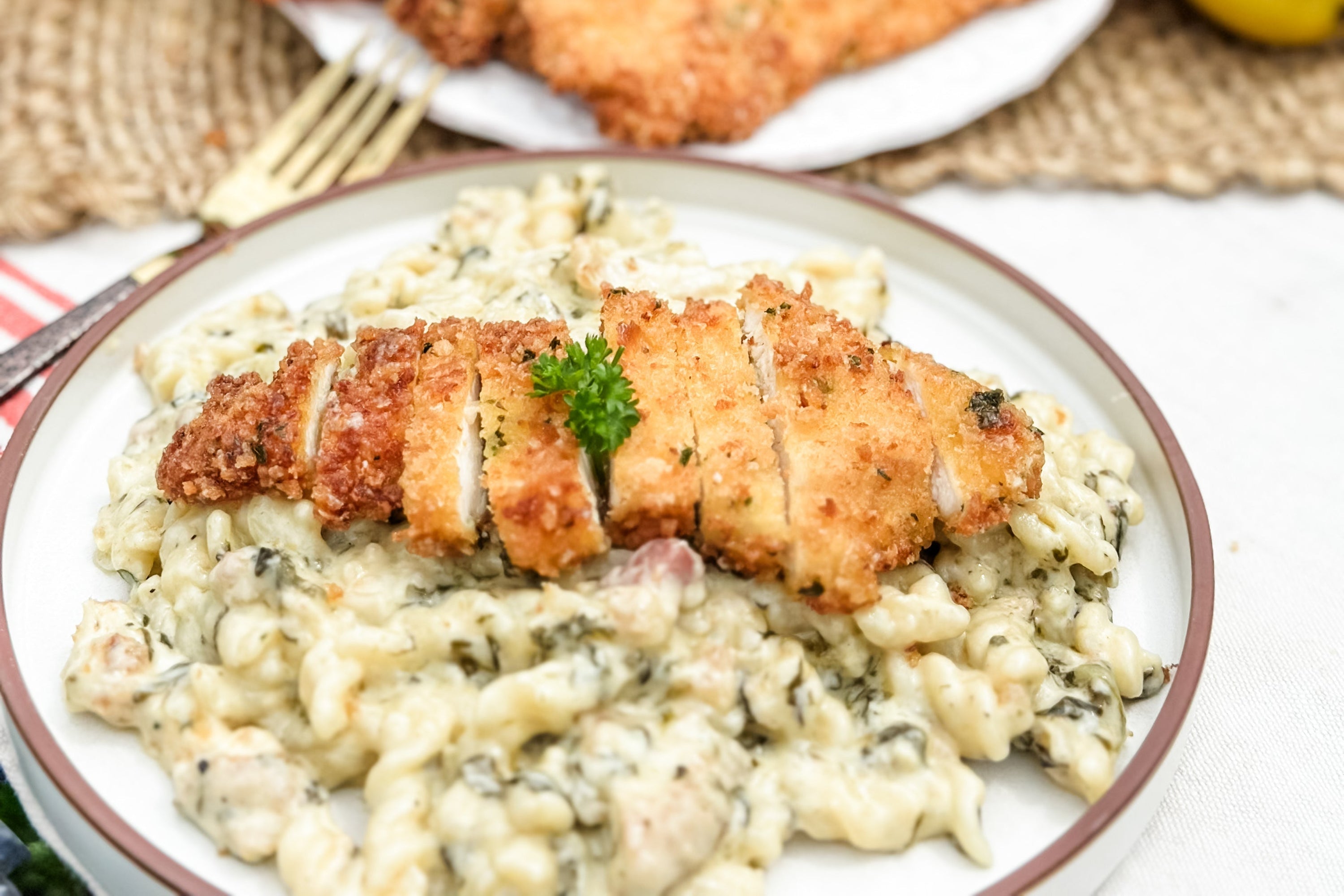 Sliced breaded chicken cutlet on creamy lemon-parmesan pasta with spinach and parsley garnish on a white plate