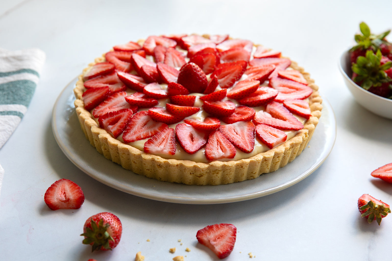 Angled overhead of Einkorn strawberry tart with sliced berries on pastry cream and golden crust on a white plate