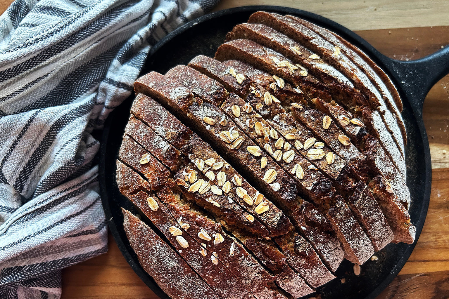 Overhead view of sliced honey oat Einkorn sourdough boule topped with oats in a cast iron skillet on a wooden board