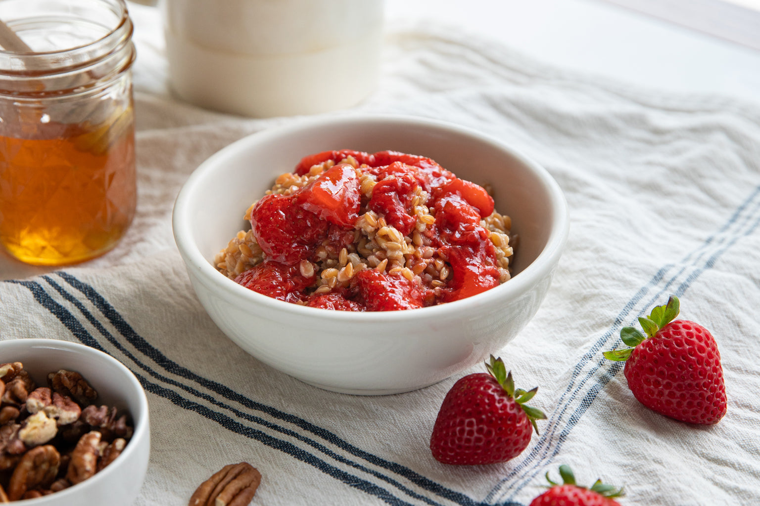 Front view of a bowl of einkorn wheat berries topped with sautéed strawberries and coconut cream on a blue-striped linen