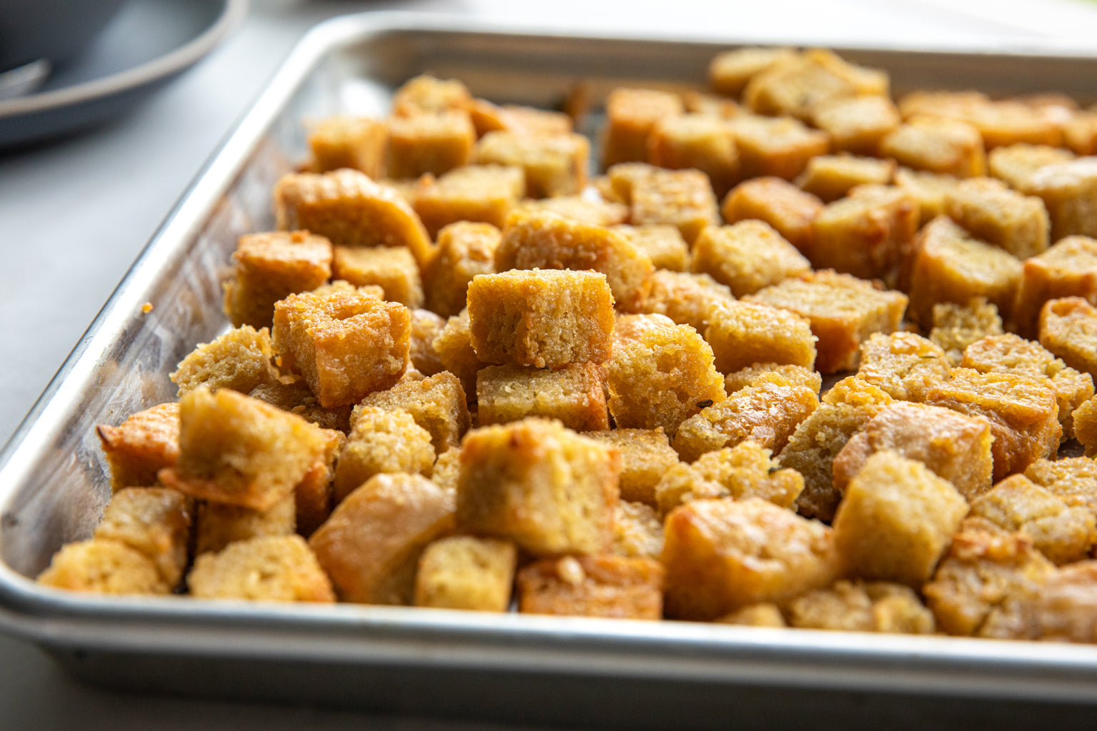 Close-up of cubed croutons made with einkorn flour, showcasing golden toasted, herby texture on a metal baking sheet