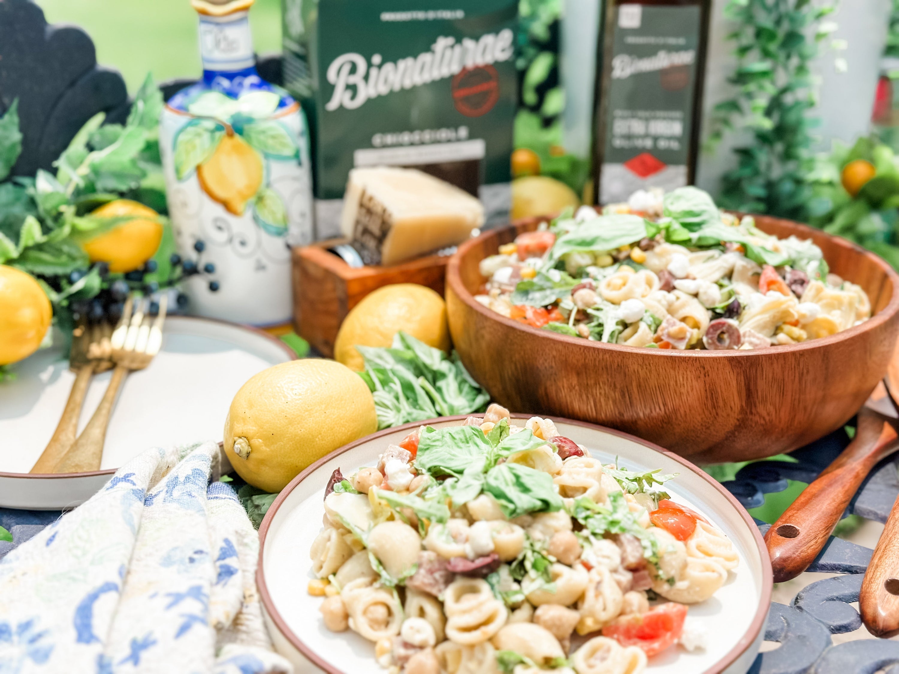 Two bowls of creamy no-mayo pasta salad served outdoors with lemons, fresh basil, and a Bionaturae box in the background