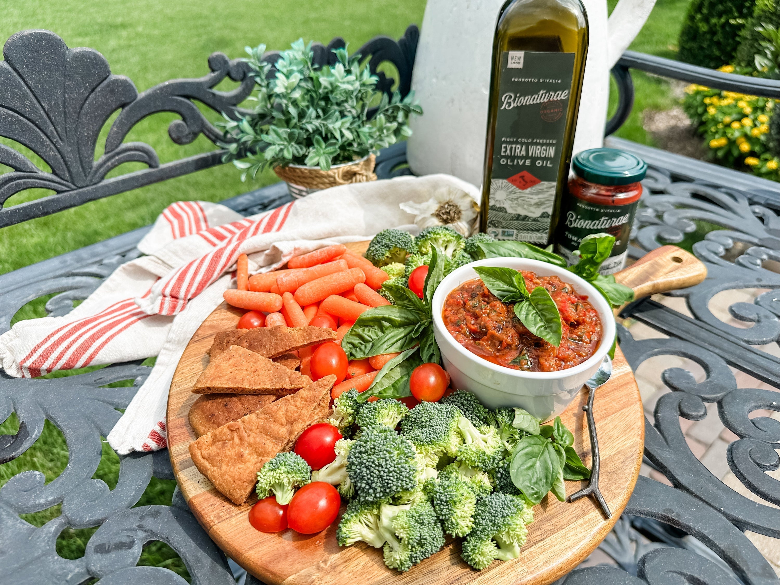 Bowl of roasted vegetable spread on a wooden board with pita chips, cherry tomatoes and Bionaturae olive oil on a table
