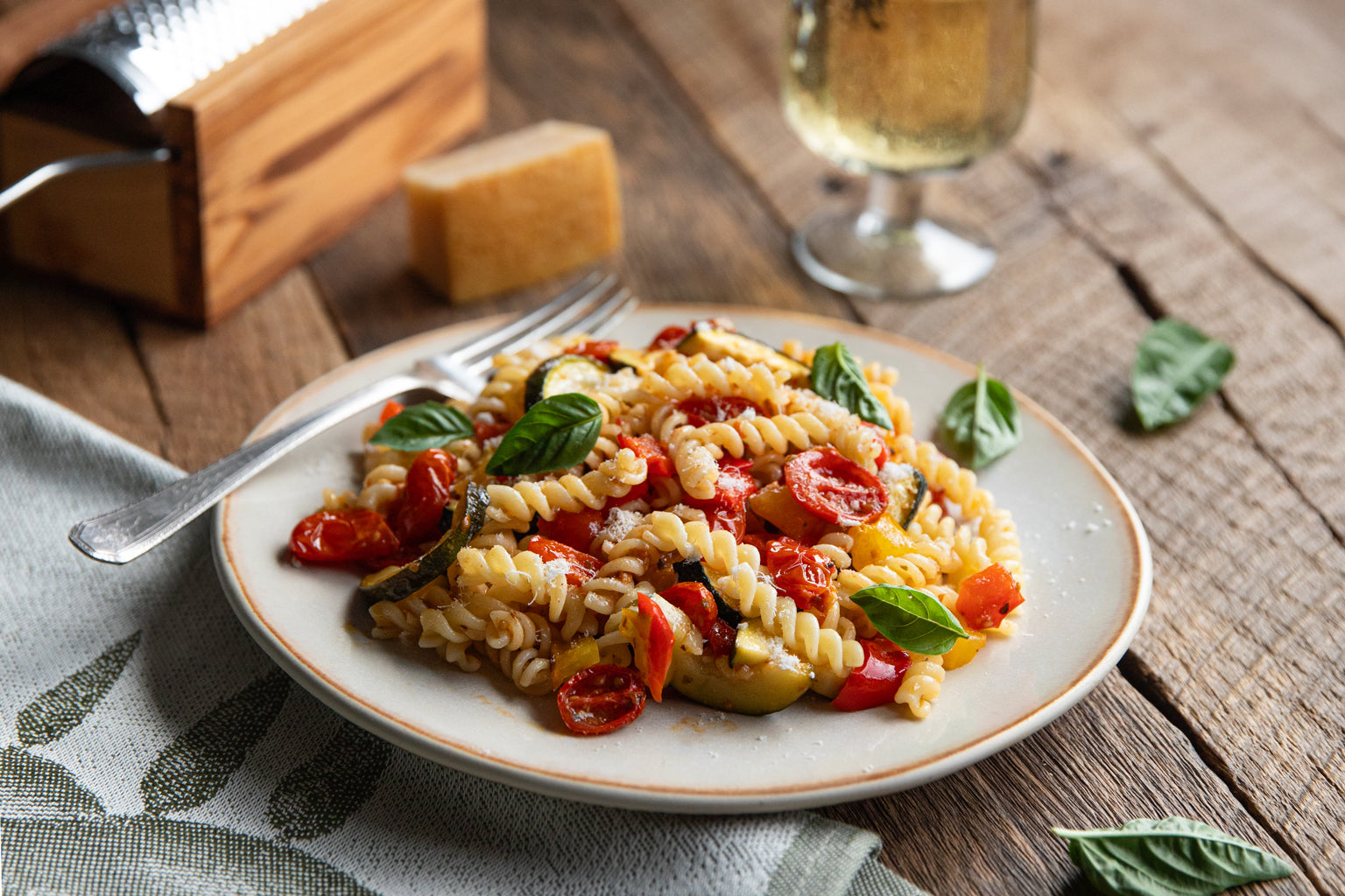 Fusilli tossed with oven-roasted cherry tomatoes and zucchini, garnished with basil on a plate on a rustic wooden table