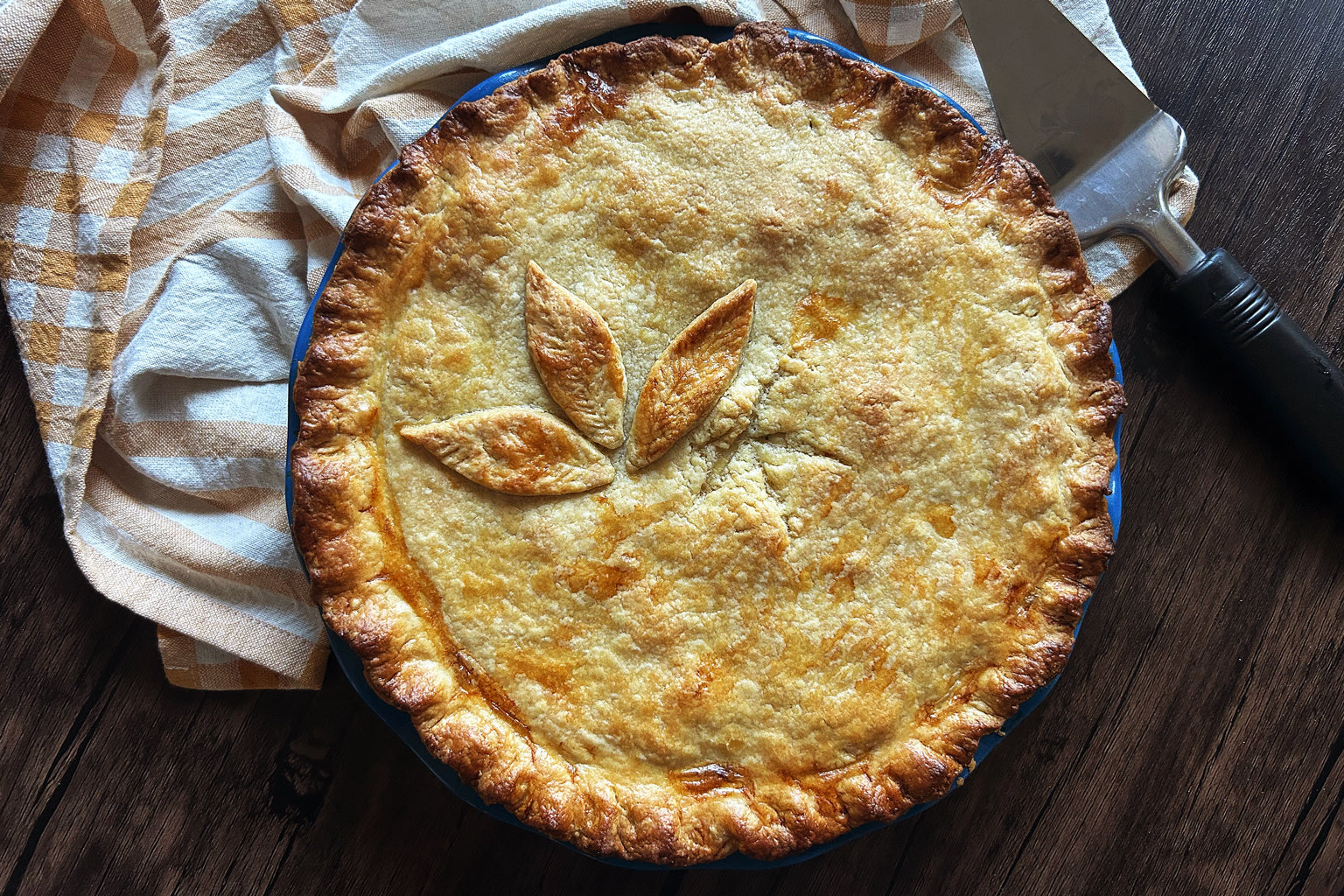 Overhead view of a golden-brown sourdough chicken pot pie with three leaf vents in a blue pie dish on a wooden table