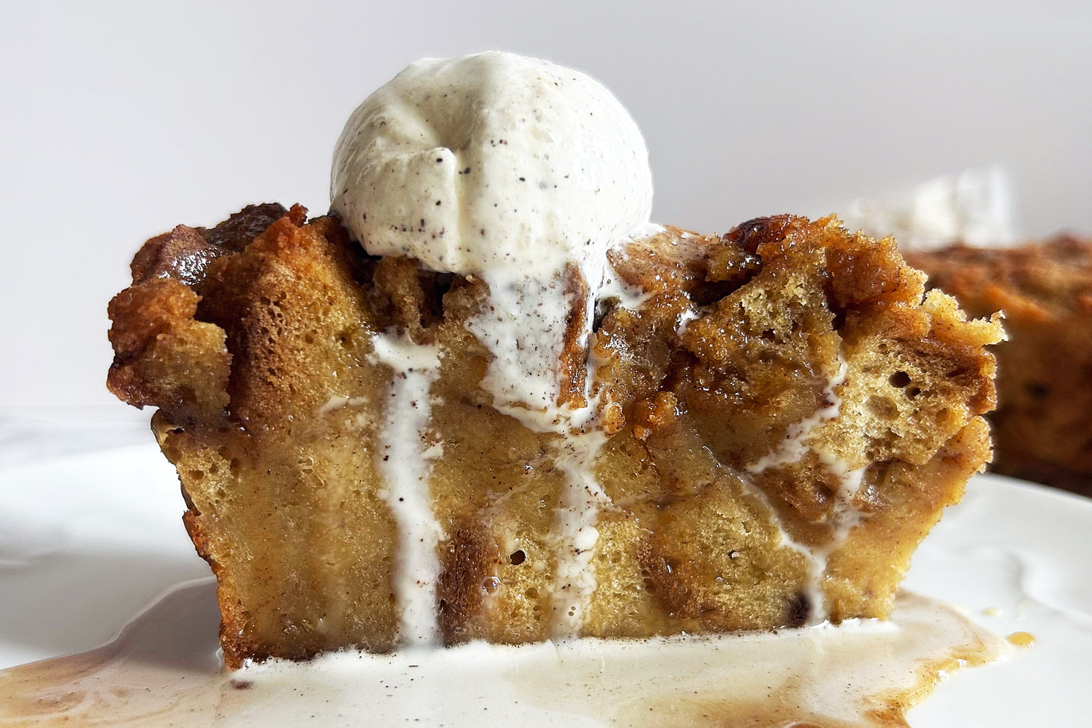Slice of maple caramel sourdough bread pudding topped with a melting scoop of vanilla ice cream and caramel sauce on a white plate