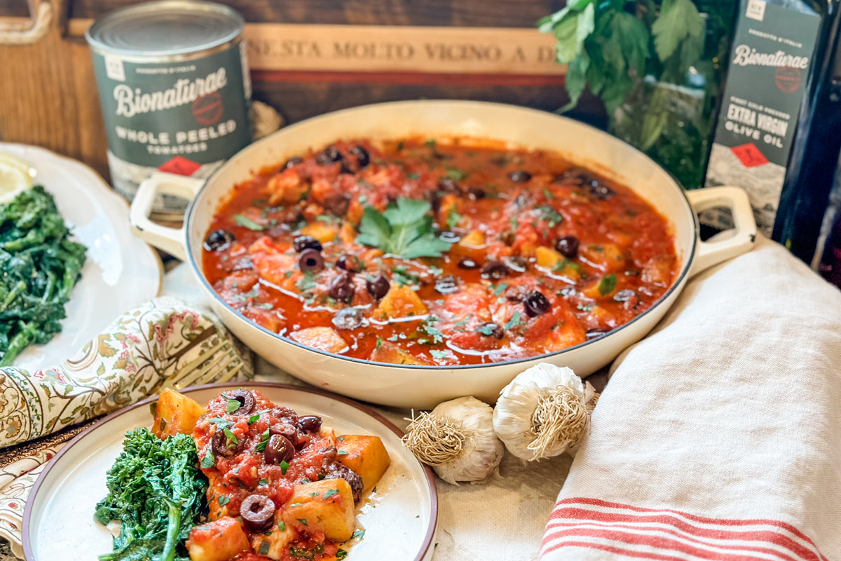 Pan of Acqua Pazza (Italian poached fish) in tomato broth with olives, served with roasted potatoes and sautéed greens