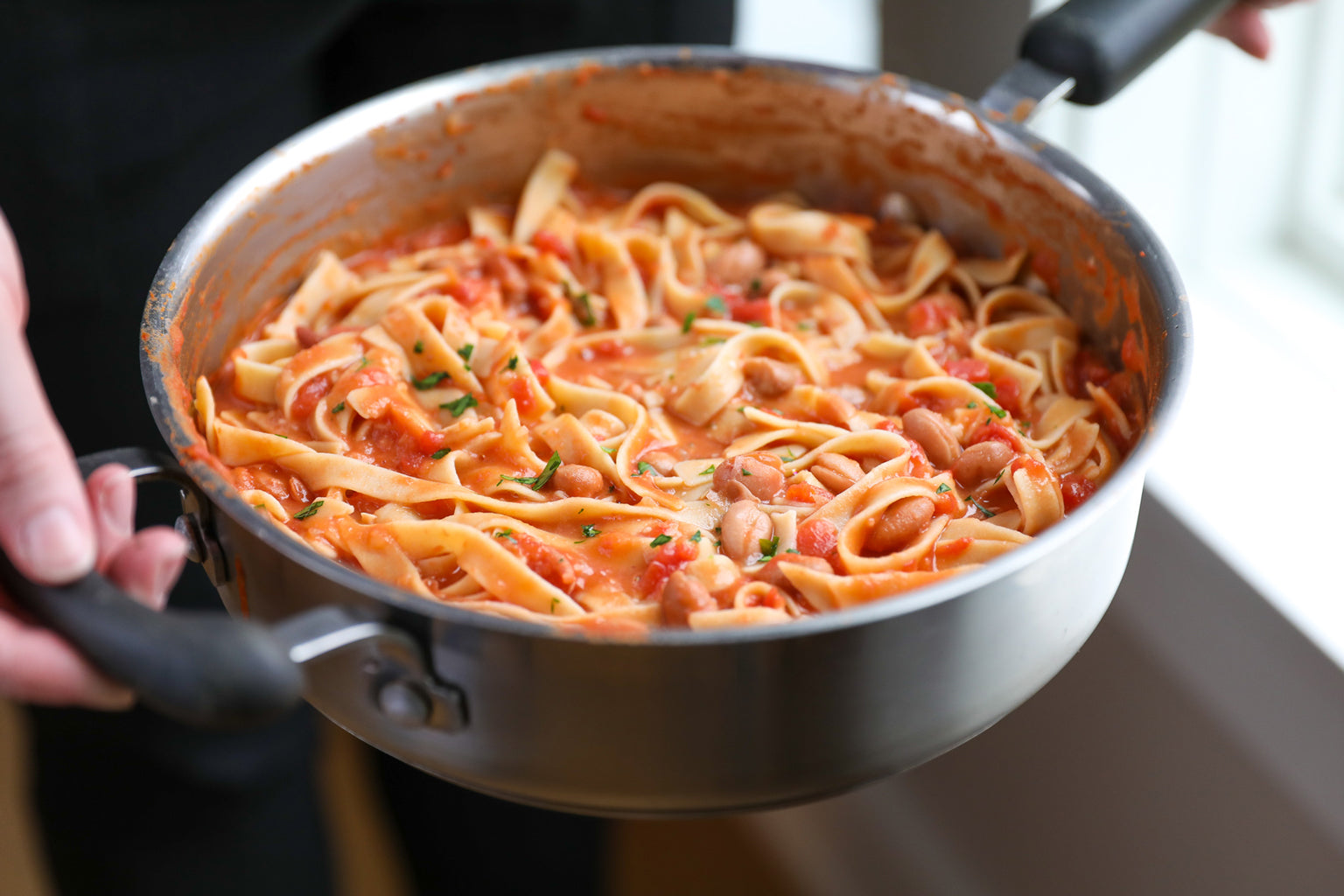 Person holding a pot of Gluten Free tagliatelle tossed in tomato and borlotti bean sauce