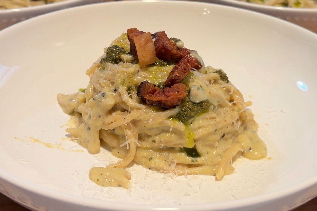 Spaghetti pesto carbonara in a white bowl, tossed in creamy sauce and topped with pesto dollops and crispy pancetta